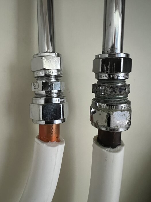 Två röranslutningar med kromade övergångsnipplar, den vänstra med en kopparledning och den högra med en mörkfärgad ledning.