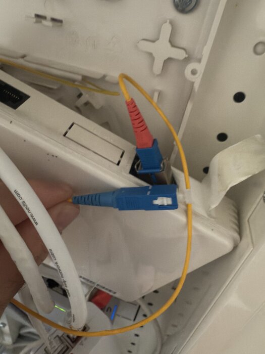 Gul fiberoptisk kabel ansluten till en mediaomvandlare med en blå kontakt och vita kablar i bakgrunden.