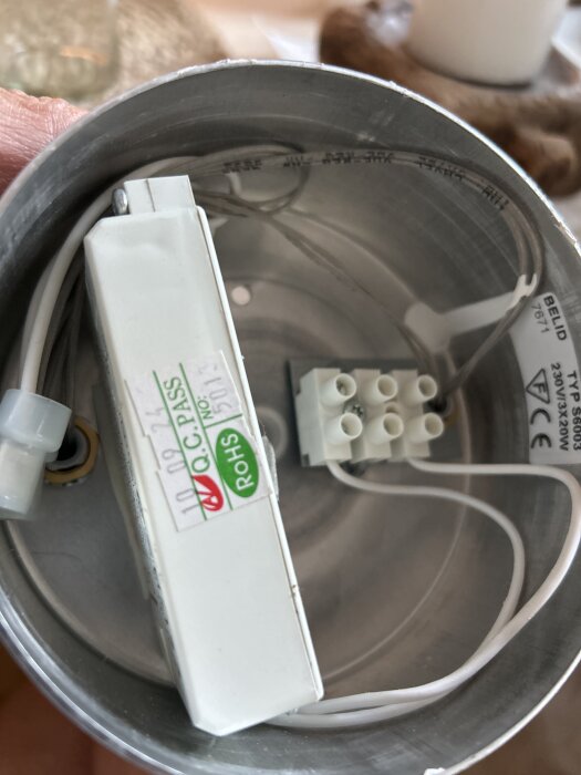 Inuti en rund lampa visas elektrisk utrustning inklusive en vit terminalblock och sladdar, samt en etikettmärkt halogenomvandlare.