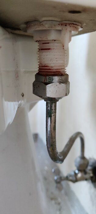 Läckande toalettkoppling med rör och mutter, antyder vattenläckage samt rost- och kalkavlagringar.