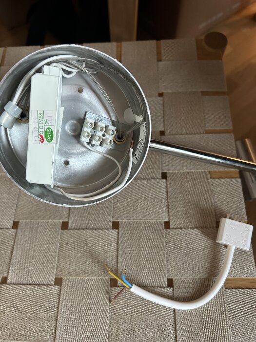 Spotlampa med halogenomvandlare och anslutningskabeln med blå och brun sladd visas bredvid en kontakt på ett golv med korsvävt mönster.