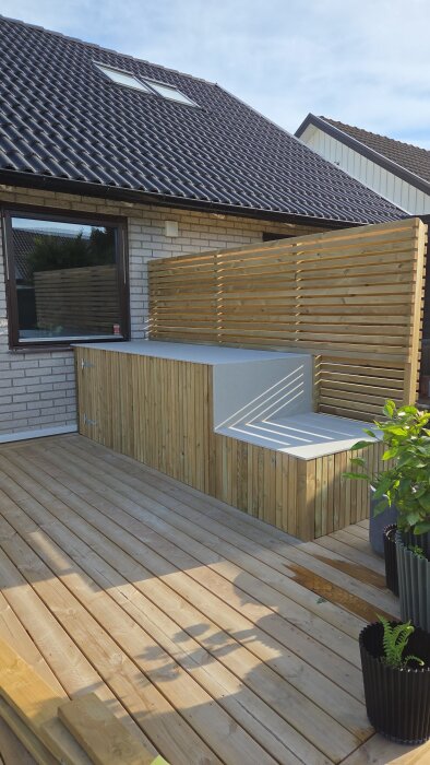 Fibercementskivor installerade på en terrass med träpaneler och trall, solbelyst med planterade växter i närheten.