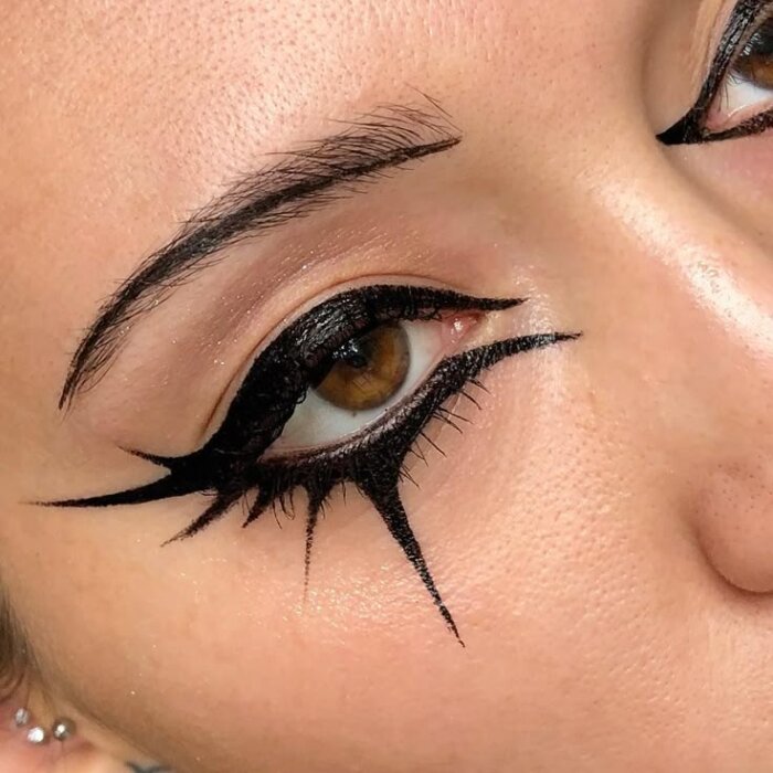 En närbild av ett öga med konstnärlig och dramatisk eyeliner-design med vingar ovan och under ögat.