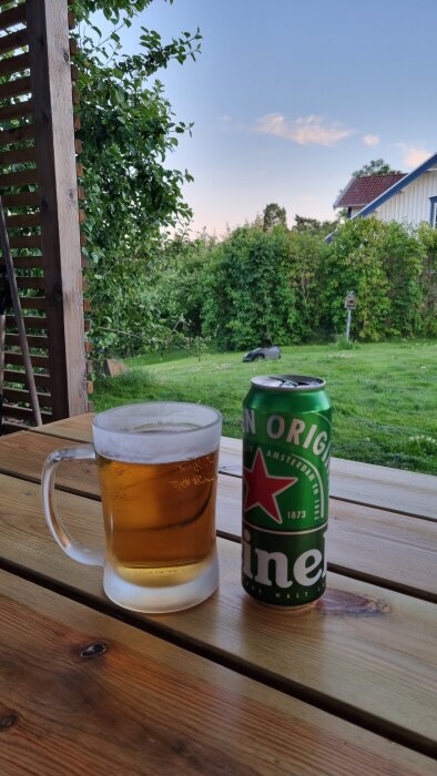 Ölglas och burk på ett träbord med grönskande trädgård och gräsklippare i bakgrunden.