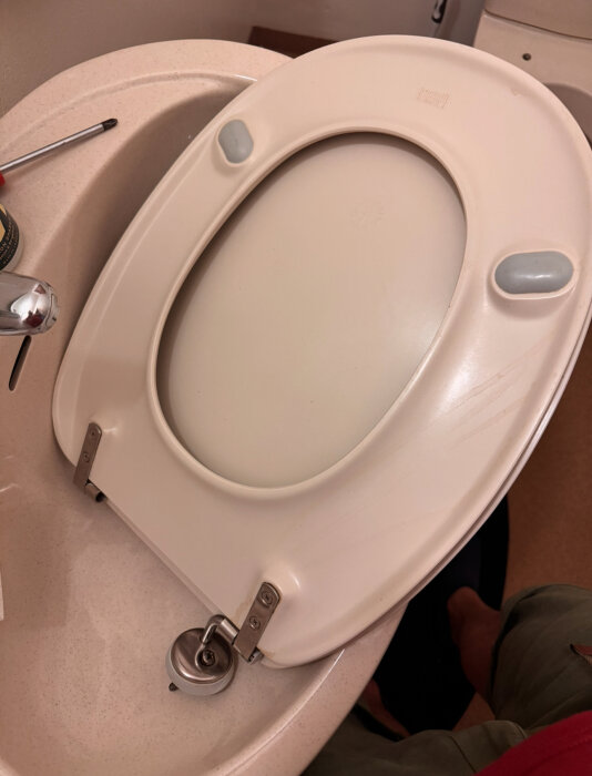 Toalettsits med saknad armfäste, märkt "Gustavsberg 82" och "380", med skruvmejsel och burk på handfatet i bakgrunden.