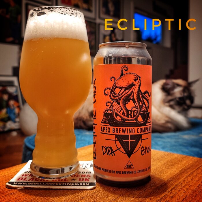 En pintglas fylld med öl bredvid en burk Apex Brewing Company öl med en bläckfisklogotyp. Ordet "Ecliptic" syns i bakgrunden.