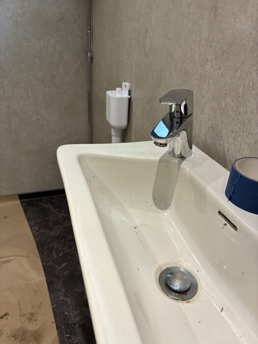 Handfat med Hansgrohe blandare mot vägg med våtrumsskiva, golv delvis täckt av papper för skydd under renovering.