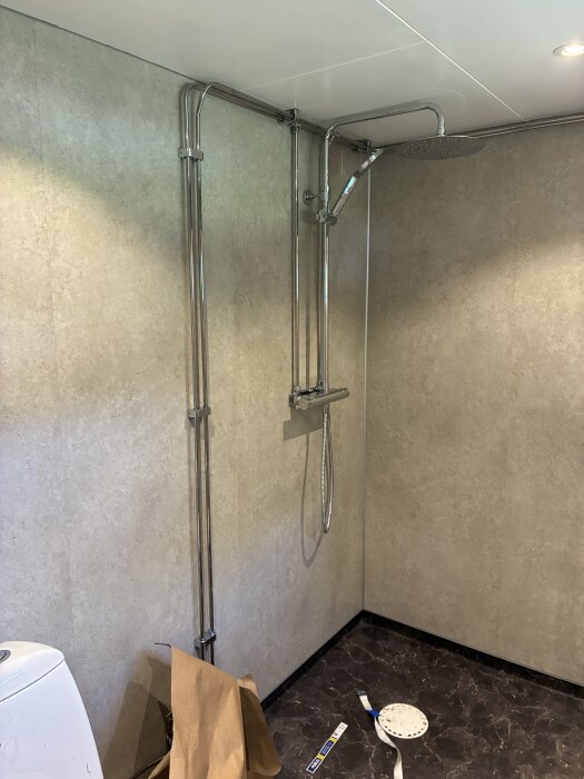 Badrum under renovering med synliga rör och duschblandare från Gustavsberg på vägg klädd med Fibo våtrumsskivor och plastmatta från Forbo på golvet.