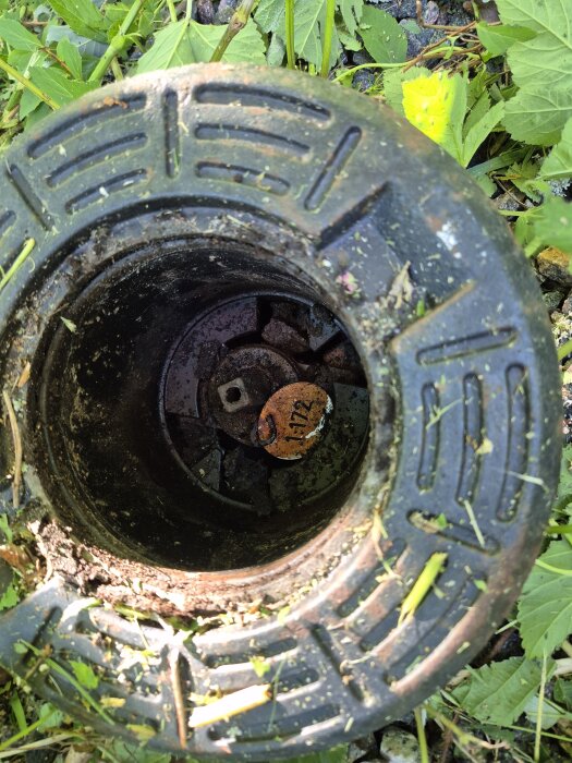 Brunnslock med orange ventilnyckel, omgiven av gräs. Ventil för avstängning av vatten utanför huset.