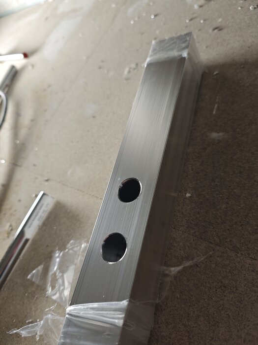 Fyrkantsrör med två runda genomföringshål, del av hemgjord rörgenomföringsprofil till duschvägg.