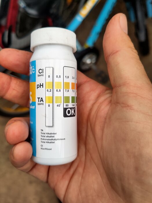Flaska med testremsor för att mäta klor, pH och alkalinitet i vatten, hålls i en hand.
