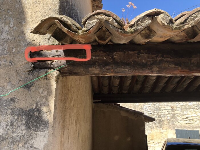 Murken bärande träbalk på äldre hus i Frankrike markerad med röd färg, delar av balken synligt skadad, möjligt behov av reparation eller utbyte.