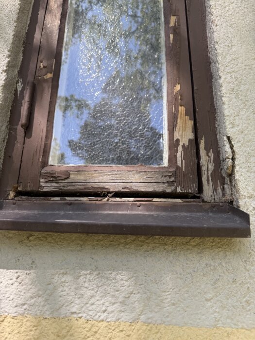 Äldre träfönster med sprucken och flagnande färg, träet är skadat och i behov av renovering.