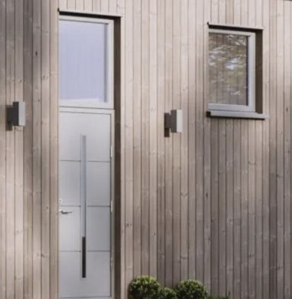 Träbeklädd husfasad med en modern vit dörr och fönster ovanför och bredvid dörren.