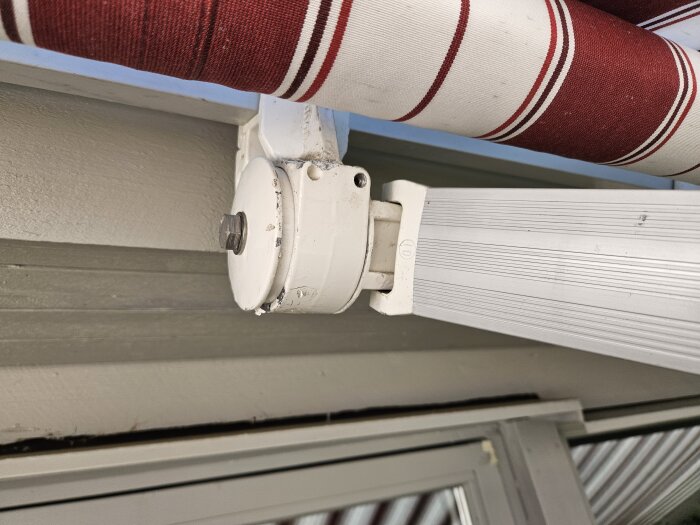 Kassett till markis med justeringsbult och sexkantsnyckel synlig, detaljerad infästning mot vägg och vit-röd mönstrad markisduk.