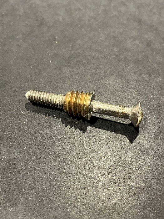 Koppelskruv i metall, används för sammanfogning av dubbelfönster. Placeras på mörk yta.