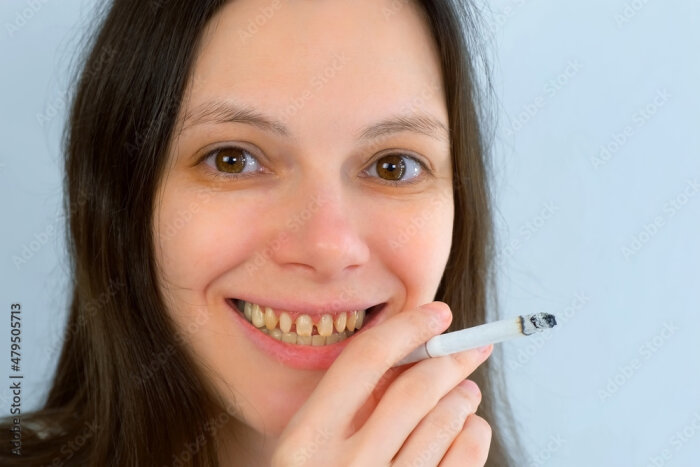 Person som håller en tänd cigarett, ler mot kameran.