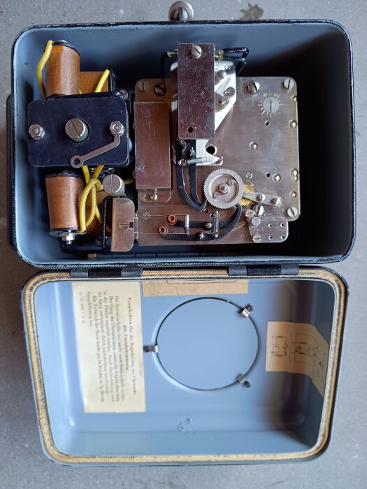 Kopplingsur från 1939 tillverkat av Telegrafverket, med synliga mekaniska komponenter i metall och plast i en blågrå låda.