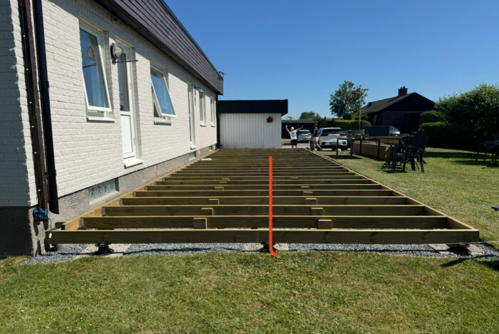 Träram för nytt trädäck under byggnation framför ett hus, med reglar som visas och en röd linje markerad i mitten av konstruktionen.