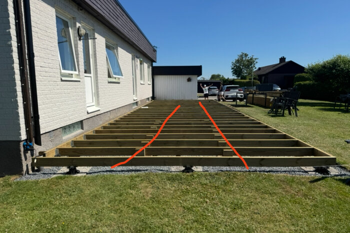 Träram för ett trädäck under konstruktion vid sidan av ett hus. Två röda linjer markerar möjliga placeringar för stödreglar.