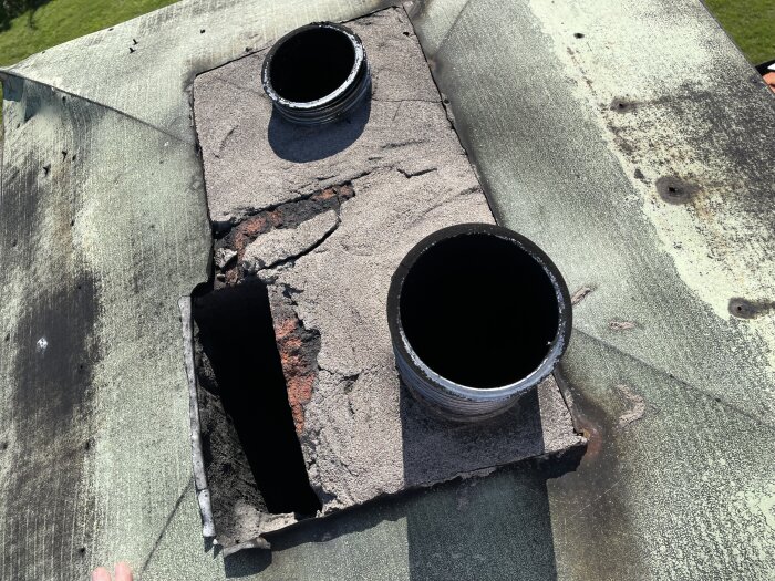 Skorstenstopp med två insatsrör, omgiven av sprucket bruk och takmaterial, fotograferad under diskussion om att ta bort insatsrör för att höja murstockens temperatur.