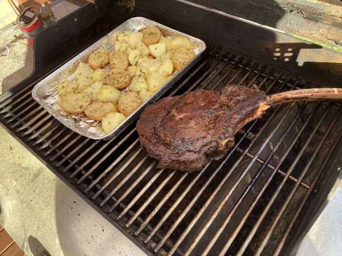 En grill med en stor köttbit och en aluminiumform med potatis och brödskivor.
