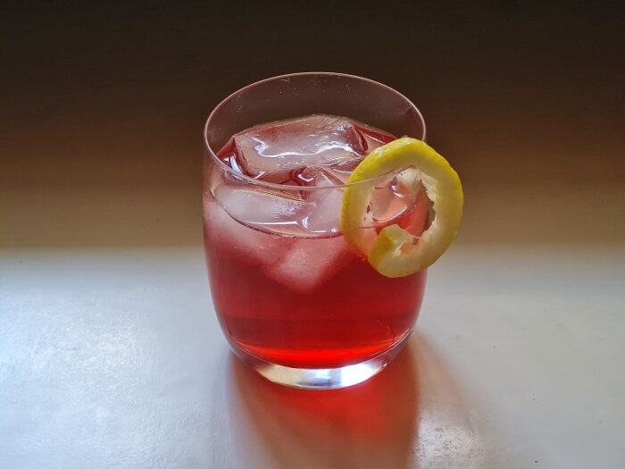 Glas med Campari, Schweppes tonic, is och citronskal pÄ en yta.