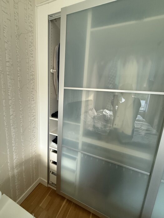 IKEA PAX garderob med skjutdörrar i sovrum, delvis öppen och visar insidan med kläder och hyllor.
