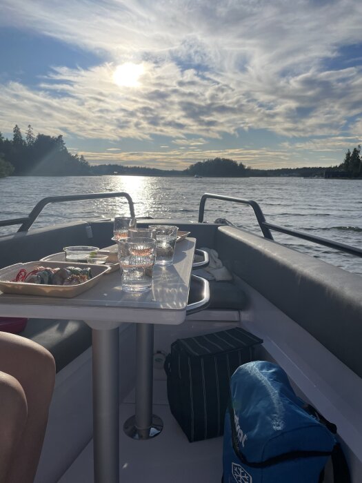BÄtutflykt med sushi och dryck pÄ bordet, solnedgÄng över vattnet i bakgrunden.