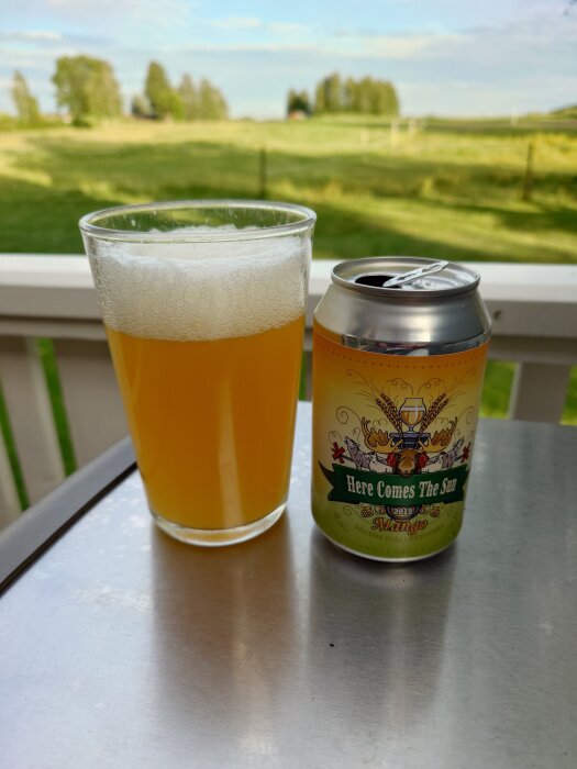 En burk och ett glas med öl på ett trädäck med grönskande bakgrund.