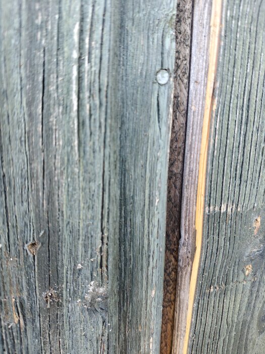 Sliten träpanel med lös färg och synlig springa, avslöjar underliggande plywood på en husfasad.
