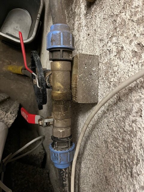 Vattenrör med blå kopplingar och kulventiler monterat på en vägg, sett från en sida.