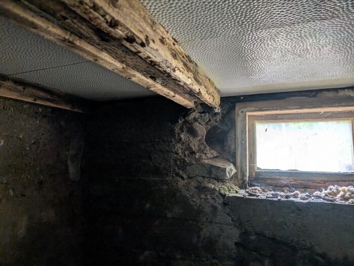 Gammalt, slitet källartak och vägg i sten med ett litet kvadratiskt fönster. Sprickor och tecken på sättningar syns i murbruket.