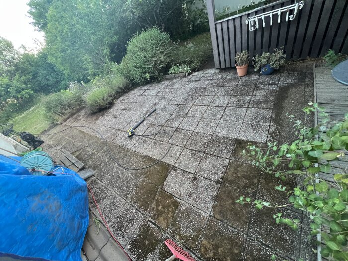 Markstenar bredvid ett hus där mossan har tagits bort, högtryckstvätten står kvar på platsen och omgivande vegetation syns runtom.