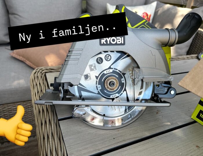 Cirkelsåg från Ryobi med etiketten "Ny i familjen" och en tummen upp-emoji i bakgrunden på en uteplats med träbord.