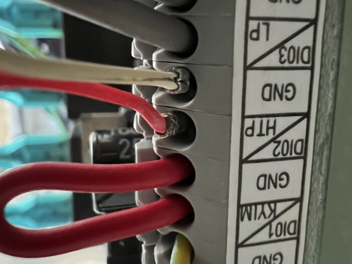 Elektriska kablar anslutna till en panel med märkningar, inklusive röd och vit kabel anslutna vid etiketten GND.