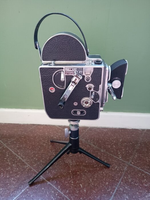 Bolex 16mm filmkamera på stativ mot grön vägg, använd för stereofotografering, stillbild tagen nära lägsta vinkeln.