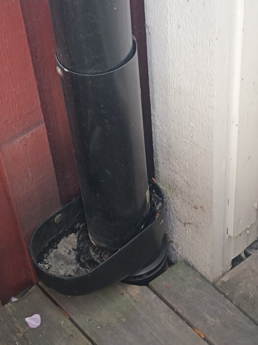 Svart stuprör vid röd och vit vägg, mynnar ut under altan, osäker koppling till dagvatten eller avlopp.