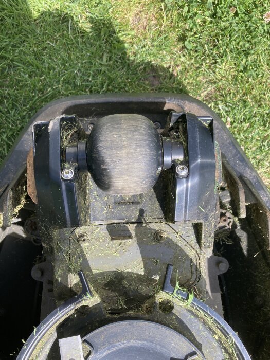 Bild på gräsklipparens hjul och botten täckt med gräsklipp. Ett av fästena verkar trasigt och smutsigt.