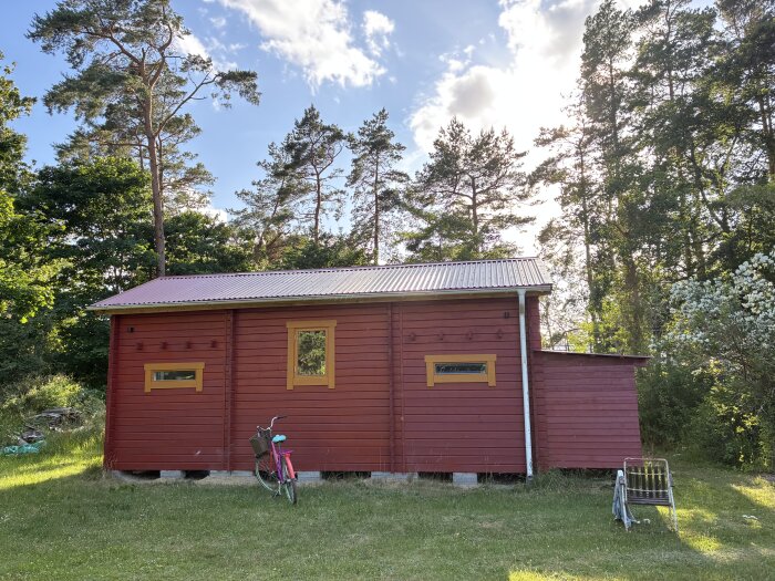 Rött timmerhus i Sorsele med gula fönster och plåttak, omgiven av träd. En rosa cykel står lutad mot väggen.