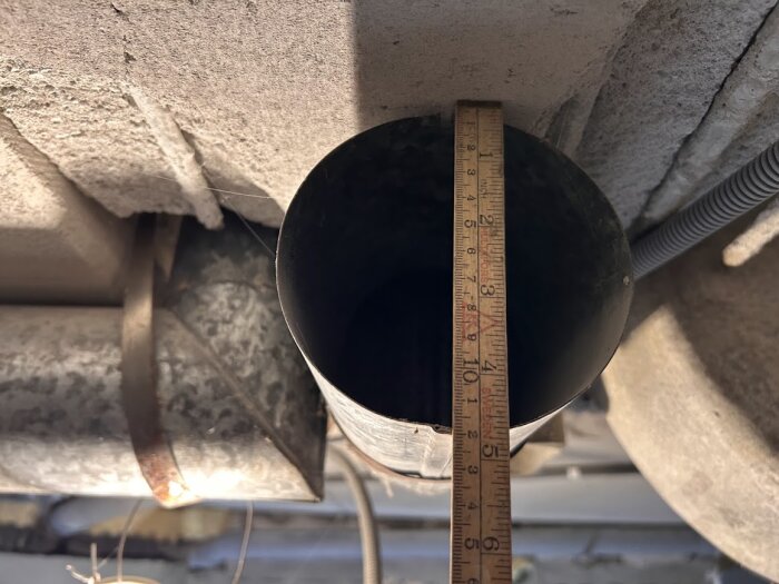 Ventilationsrör i en källare mäts med linjal; diameter ca 120 mm.