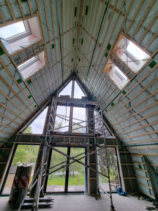 Isolerat innertak i ett trebent hus med stora fönster, ställning och byggmaterial synligt, redo för provtryckning innan fortsatt arbete.