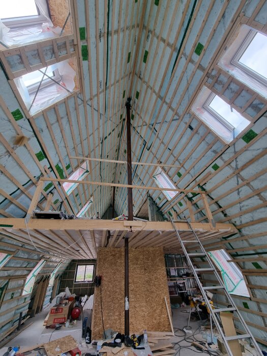 Isolerat tak och väggar i ett byggprojekt, träreglar och verktyg synliga, arbetsplats med stege och förnödenheter.