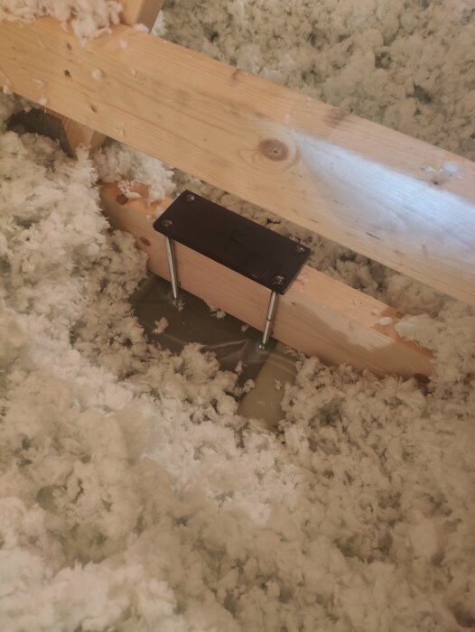 Ett träbjälke och isoleringsmaterial i ett garage, med en metallplatta och skruvar monterade för upphängning i taket.