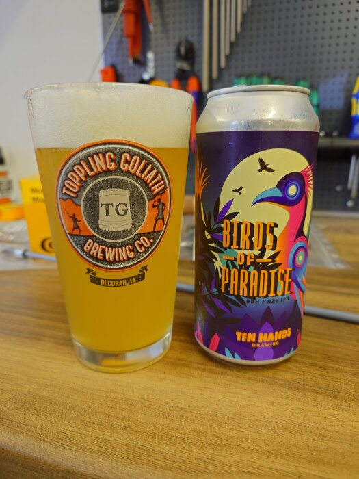 Ett glas öl från Toppling Goliath Brewery och en burk Birds of Paradise DDH Hazy IPA framför ett verktygsbord i ett garage.