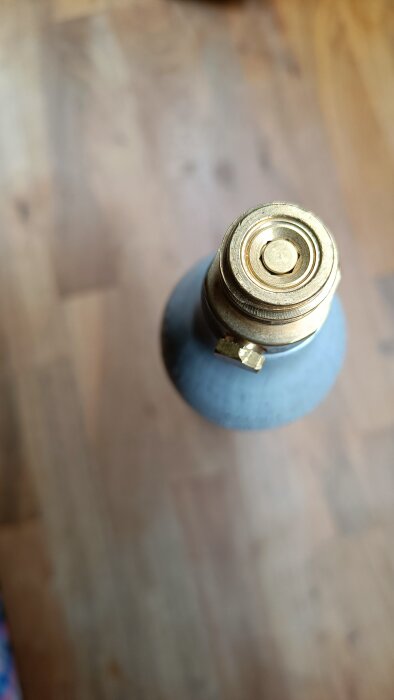 Toppen av en kolsyrepatron med gängad anslutning, placerad på ett golv. Kolsyreproblem har diskuterats i texten.