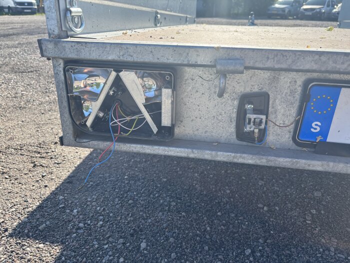 Baklykta på ett släp utan glas med synliga kablar och en EU-registreringsskylt bredvid.