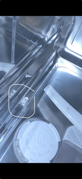 Närbild av inuti en diskmaskin med fokus på en liten grå plastventil nere till vänster och filtersystem.