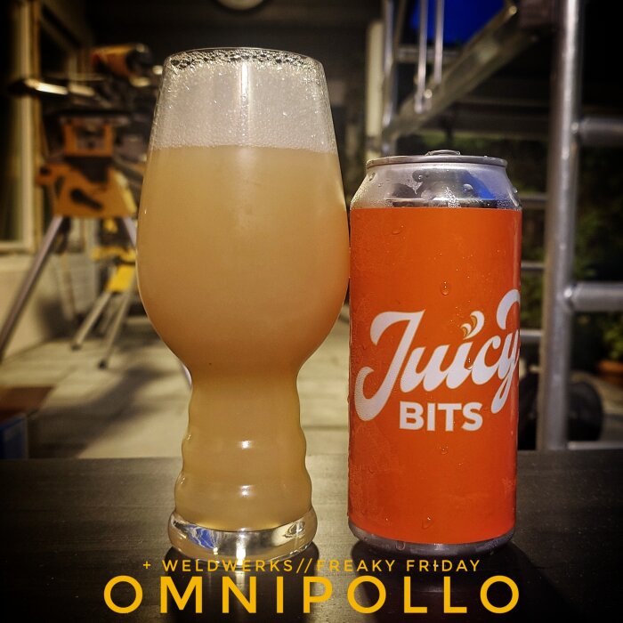 Glas med skummande öl bredvid en burk med texten "Juicy Bits" på ett bord, verktyg i bakgrunden.