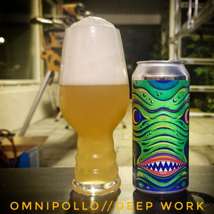 Ett glas öl med mycket skum bredvid en färgglad burk med titeln "Omnipollo//Deep Work", i en utomhusmiljö på kvällen.